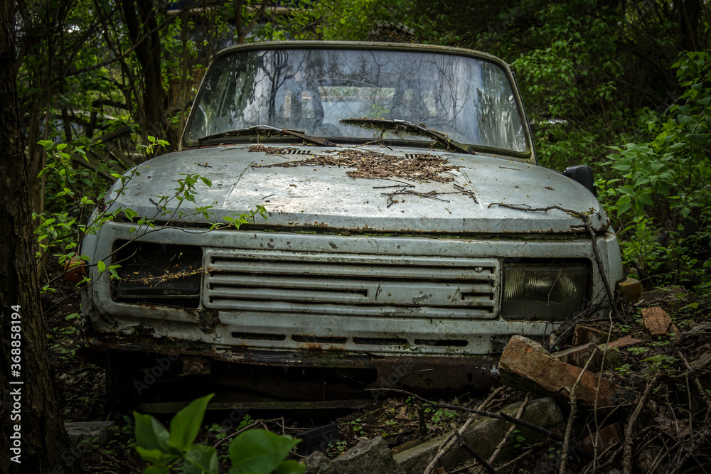 An abandoned car standing in a forest parking lot among other abandoned vehicles An abandoned car standing in a forest parking lot among other abandoned vehicles