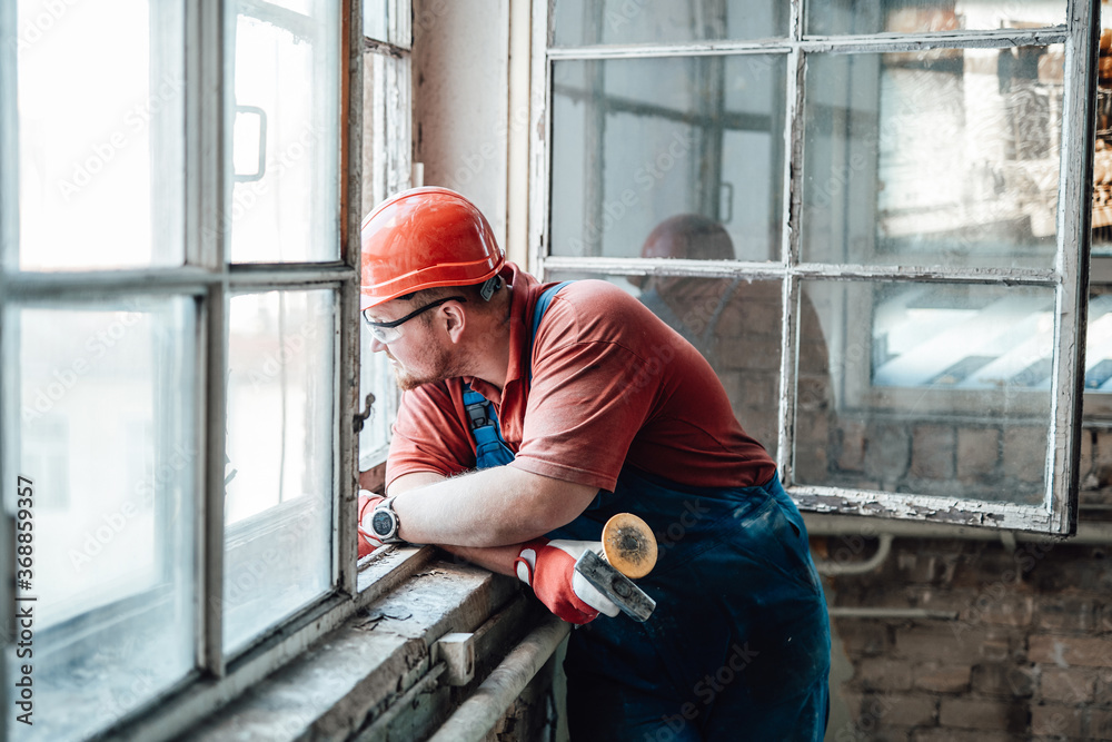 A tired builder looks out of the window of an old building, where he works as a contractor