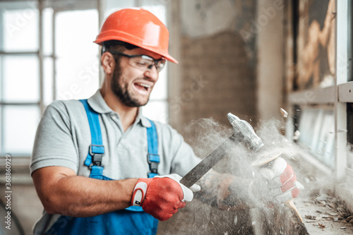 Bilde på lerret Builder, working, destroys a wall with his hammer, screaming and smiling