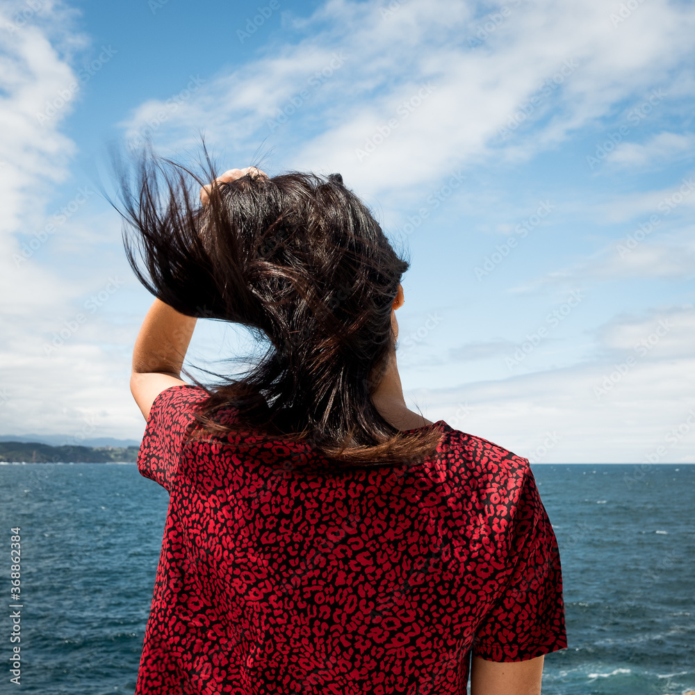 Mujer hispana de mediana edad junto al mar, pensativa mira el horizonte, asturias españa.