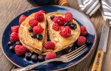 Sliced sweet homemade pancakes with raspberries and blueberries on blue plate.