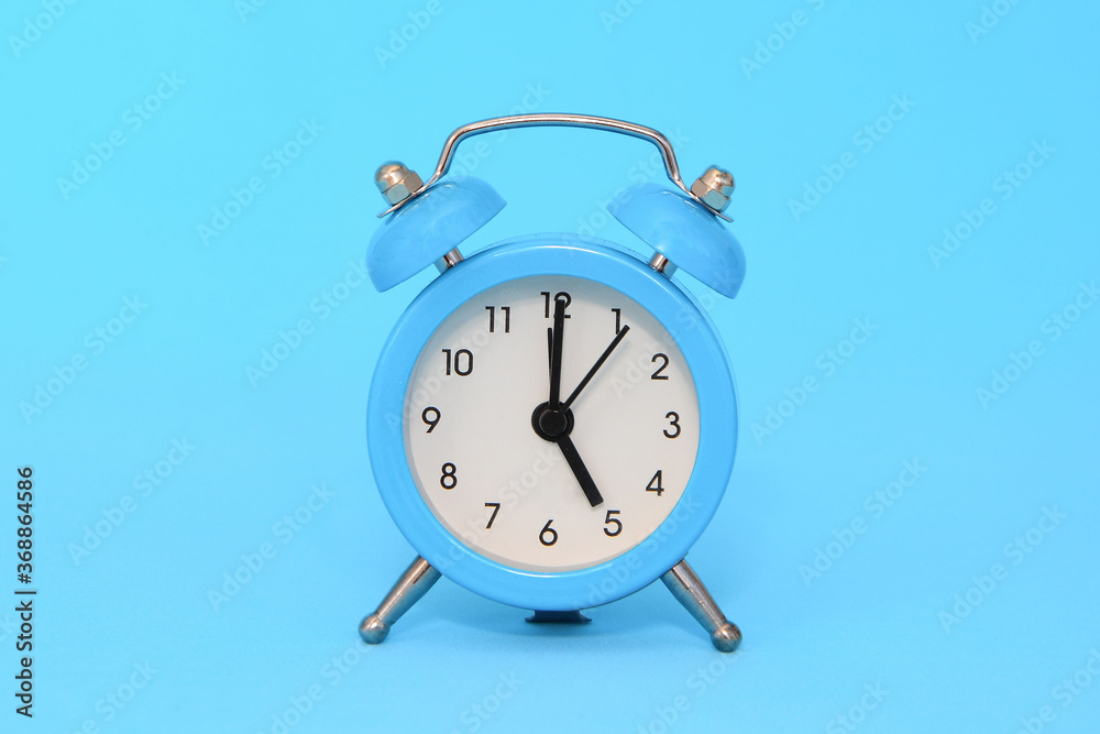 Blue alarm clock on blue background close up. 5 a.m., 5 p.m. Time concept. Blue alarm clock on blue background close up. 5 a.m., 5 p.m. Time concept.