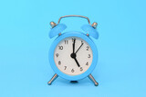 Blue alarm clock on blue background close up. 5 a.m., 5 p.m. Time concept.