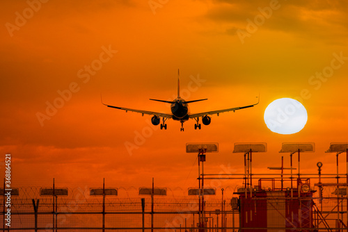 Silhouette of airplane during landing in front of amazing evening sky with sun, space for text