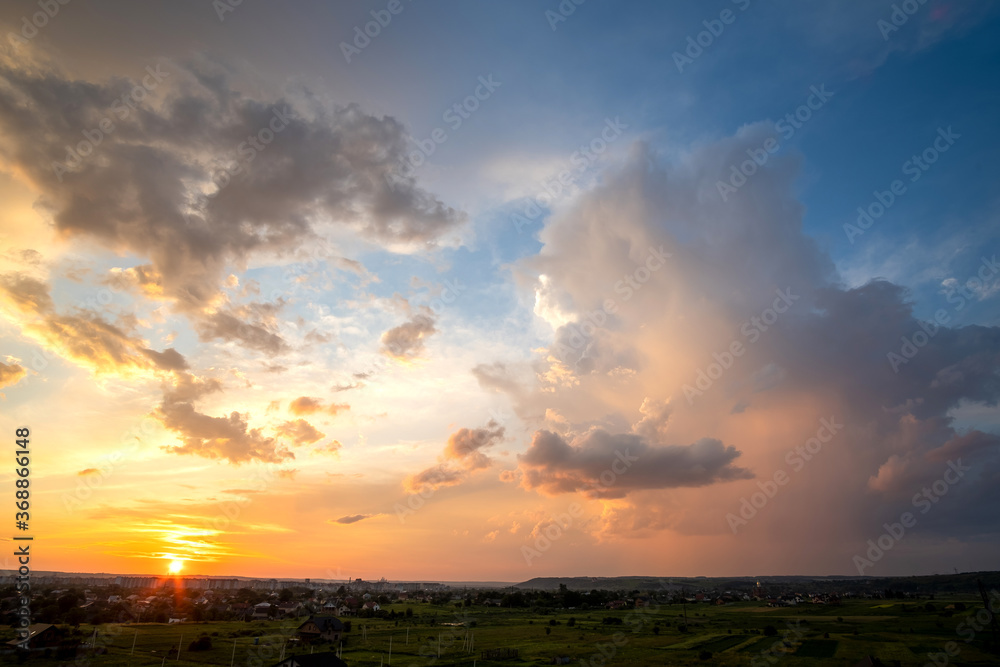 Dramatic sunset over rural area with stormy clouds lit by orange setting sun and blue sky. Dramatic sunset over rural area with stormy clouds lit by orange setting sun and blue sky.
