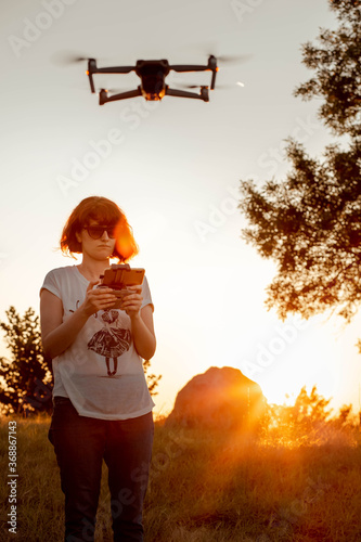 Young woman flying drone in the park. Sunset light