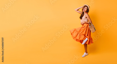 Magnificent woman in long bright skirt dancing in studio. Carefree inspired female model posing with pleasure on yellow background.