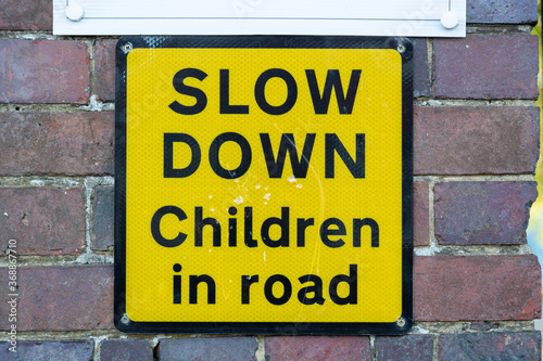 Fotografie a yellow sign on a brick wall outside a school stating slow down children in roa