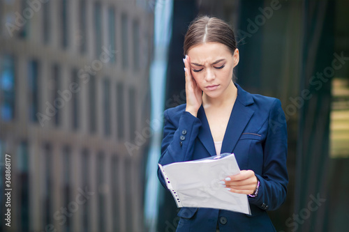 Exhausted tired frustrated businesswoman, beautiful young girl, lady looking at document, papers with sad negative look. Gorgeous woman suffering from headache, migraine holding her head with hand.
