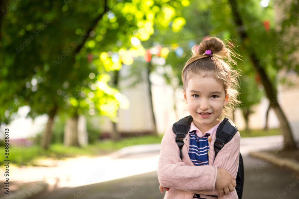 A little girl of Caucasian appearance in a school uniform with a backpack looks into the frame. Concept back to school. Elementary school, developing activities for preschoolers. Space for text A little girl of Caucasian appearance in a school uniform with a backpack looks into the frame. Concept back to school. Elementary school, developing activities for preschoolers. Space for text