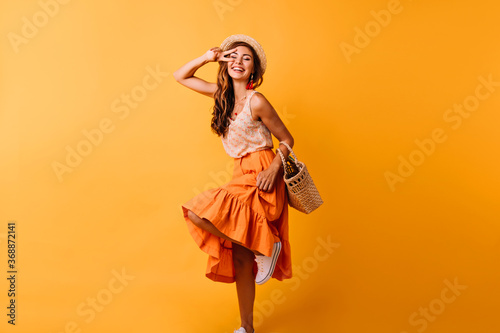 Fascinating red-haired lady expressing positive emotions. Happy ginger girl in orange skirt dancing with smile.