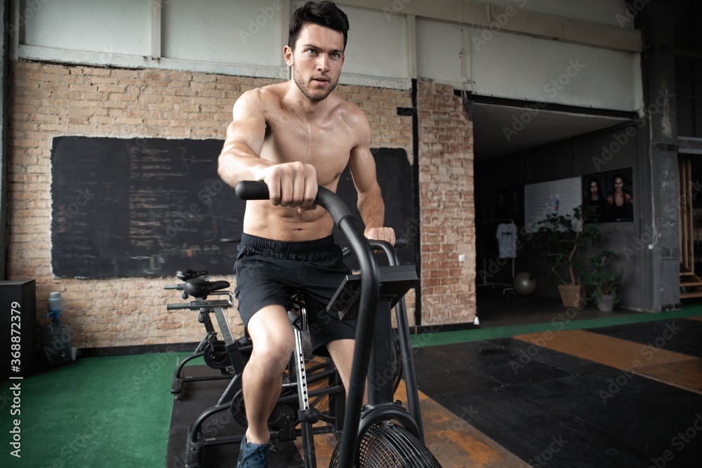 Obraz premium Man using exercise bike at the gym. Fitness male using air bike for cardio workout at Functional training gym.