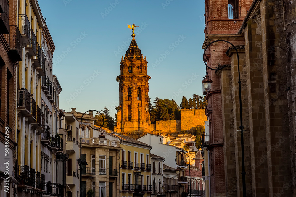 A view down the main street of Antequera, Spain towards the bell tower of the Saint Sebastion church illuminated by the setting sun in summertime