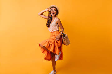 Gorgeous red-haired white woman dancing in studio. Dreamy girl in long skirt having fun on orange background.