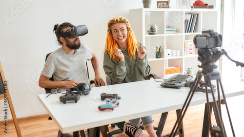 Man wearing vr glasses, while woman talking to camera. Young male and female technology blogger recording video blog or vlog about new gadgets at home