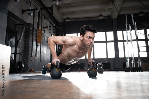 Fototapeta Naklejka Na Ścianę i Meble -  Handsome muscular man doing pushup exercise with dumbbell in a crossfit workout