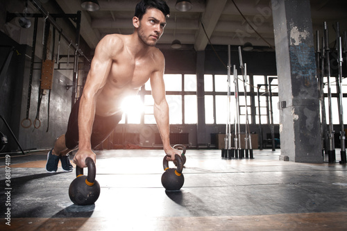 Handsome muscular man doing pushup exercise with dumbbell in a crossfit workout