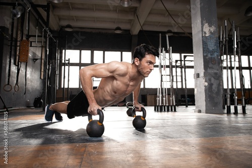 Handsome muscular man doing pushup exercise with dumbbell in a crossfit workout