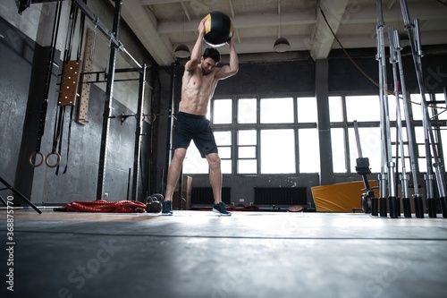 Foto Fit man throwing medicine ball doing ball slam against gym floor or shoulder press upper body workout exercise