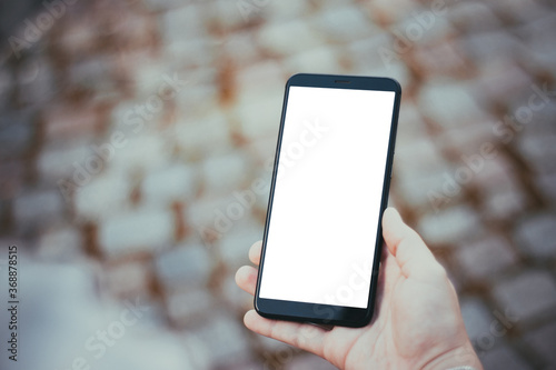 Man holding smartphone with isolated white screen on paving stones background. Mockup.