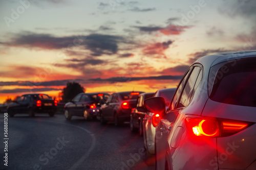 cars with their lights on stand in line in front of the barrier against the background of a summer sunset sky with clouds