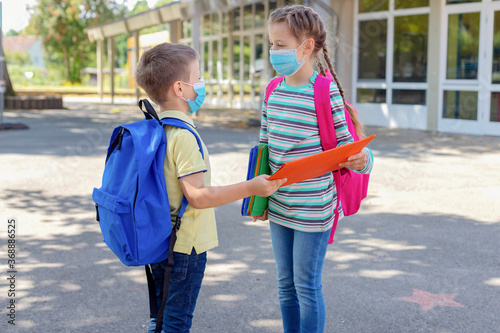 Back to school. Brother and sister or boy and girl wearing protective medical masks in the schoolyard. Distance in a pandemic. Study after the virus, vacation. Start of the school year