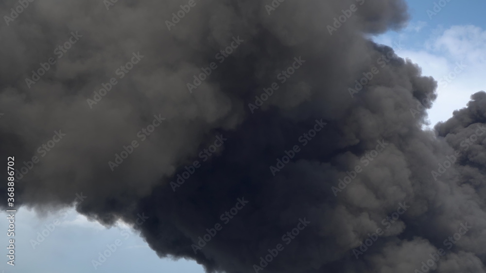 Black smoke rises above the buildings. A big chemical fire at a factory building. Thick black smoke covers the sky.