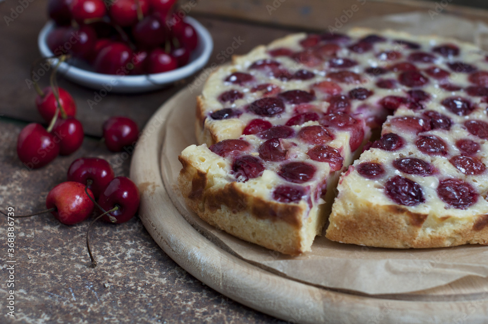 Tart with ripe sweet cherries on wooden circle board on brown background. Homemade dessert with ripe sweet cherries. Tart with ripe sweet cherries on wooden circle board on brown background. Homemade dessert with ripe sweet cherries.