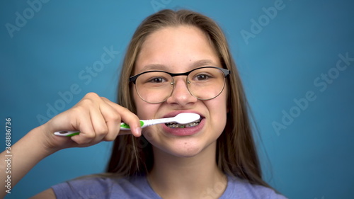 Girl with braces brush her teeth with a toothbrush closeup. A girl with colored braces on her teeth keeps her teeth clean.