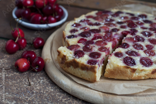 Tart with ripe sweet cherries on wooden circle board on brown background. Homemade dessert with ripe sweet cherries. 