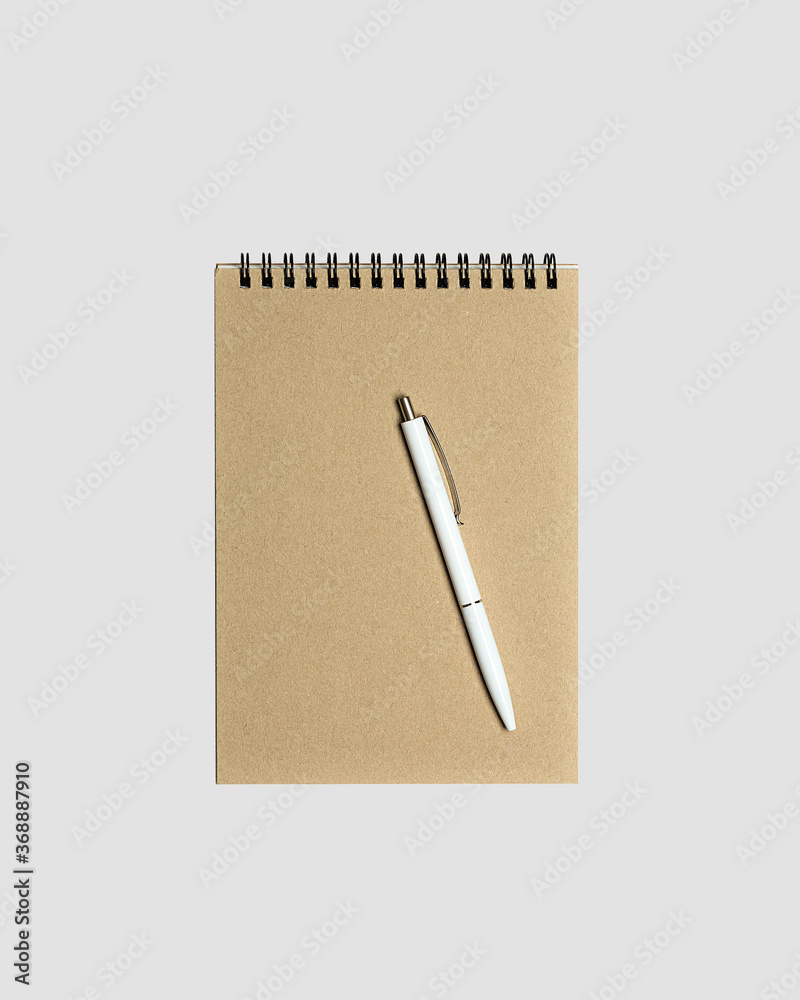 Blank spiral notepad mockup template with kraft paper cover with white glossy pen isolated on light gray background. Blank spiral notepad mockup template with kraft paper cover with white glossy pen isolated on light gray background.