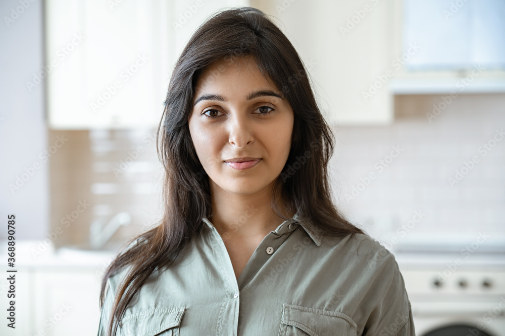 Confident young pretty indian ethnicity woman looking at camera alone at home in kitchen. Happy beautiful millennial hindu lady housewife in India indoors, close up face front headshot portrait. Confident young pretty indian ethnicity woman looking at camera alone at home in kitchen. Happy beautiful millennial hindu lady housewife in India indoors, close up face front headshot portrait.