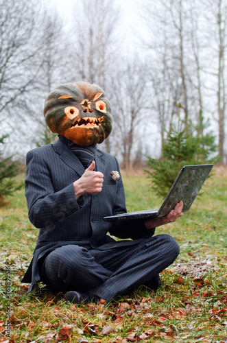 a Halloween Scarecrow with a pumpkin on his head likes what is happening on the laptop screen, or he is happy with the good quality of communication and gives a thumbs up in approval