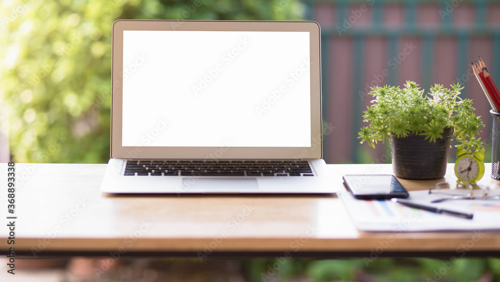 Fototapeta premium Laptop with phone and stationary on wooden table blurred garden background, selective focus.