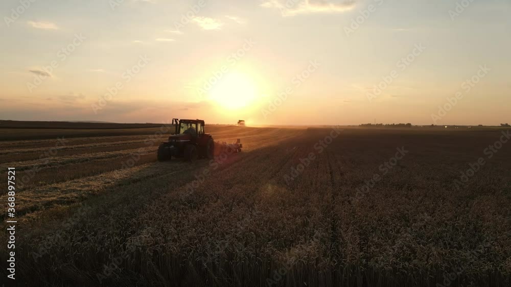Drone view: A tractor cultivates the land after a combine harvester working in a wheat field at sunset. Organic farming. Theme of agriculture, harvest season Drone view: A tractor cultivates the land after a combine harvester working in a wheat field at sunset. Organic farming. Theme of agriculture, harvest season