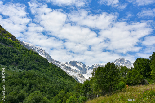 A beautiful view of the snow-capped mountain peaks of the Caucasus Mountains. White clouds against the blue blue sky.