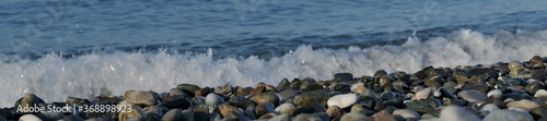 Three diagonal lines of pebble shore, sea foam and blue green water.