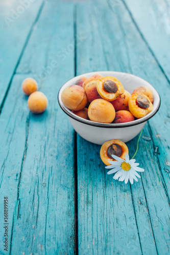ripe juicy homemade apricots with cracks and flaws in the plate and scattered on a bright turquoise wooden cover with chamomile. Harvest 2020