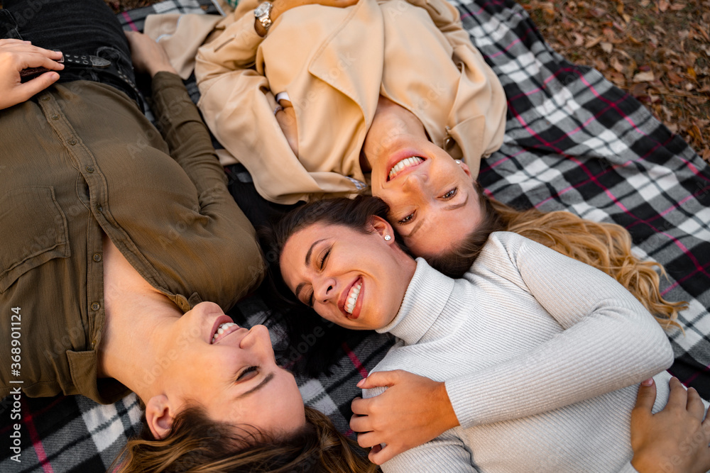 Girlfriends laying on blanket and smiling, having fun, autumn season Girlfriends laying on blanket and smiling, having fun, autumn season