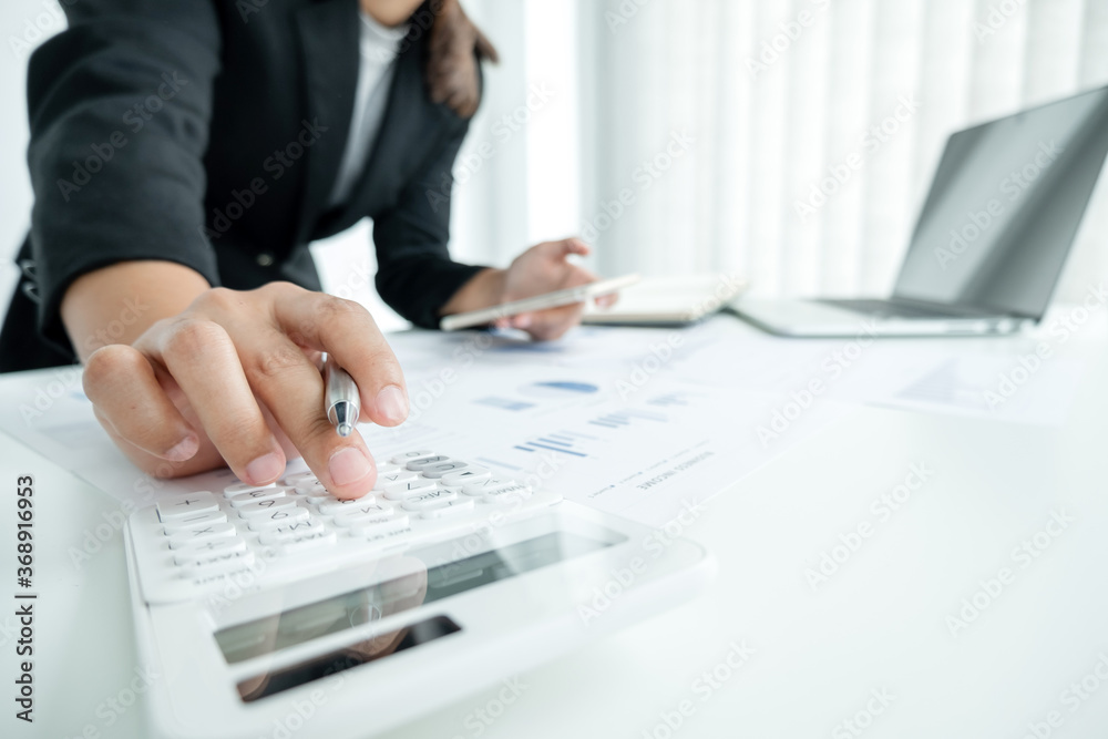 The hands of a male businesswoman use the calculator are analyzing and calculating the annual income and expenses in a financial graph that shows results To summarize balances overall in office The hands of a male businesswoman use the calculator are analyzing and calculating the annual income and expenses in a financial graph that shows results To summarize balances overall in office