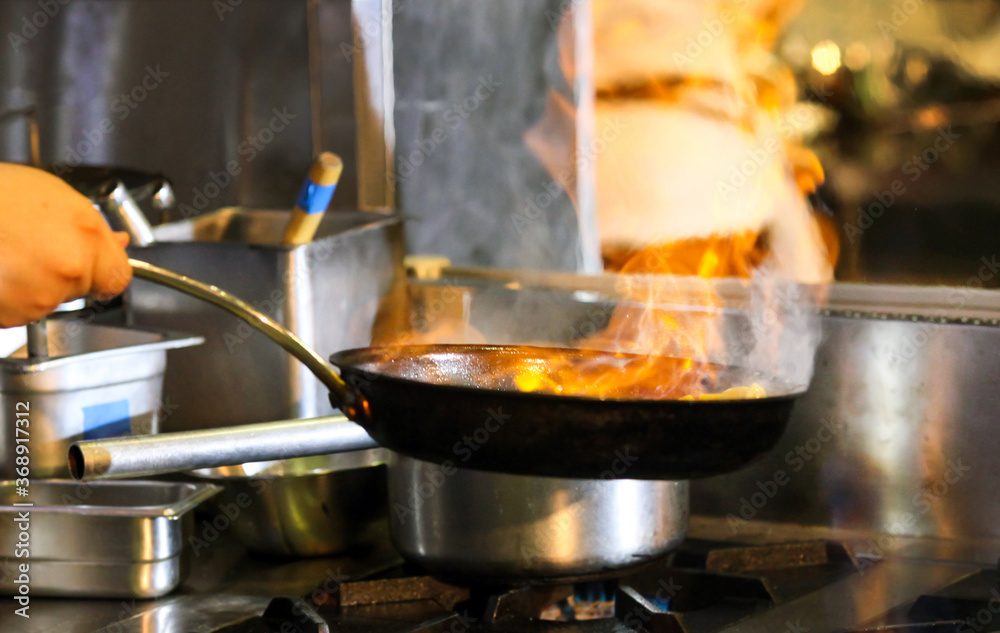 Chef cooking with flame in a frying pan on a kitchen stove.
