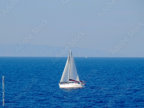 Tourists sail a yacht near the coastline of Paros Island in Aegean Sea in Greece. Paros located at the heart of the? Cyclades, one of famous Greek travel destinations for tourism and vacation. © isparklinglife