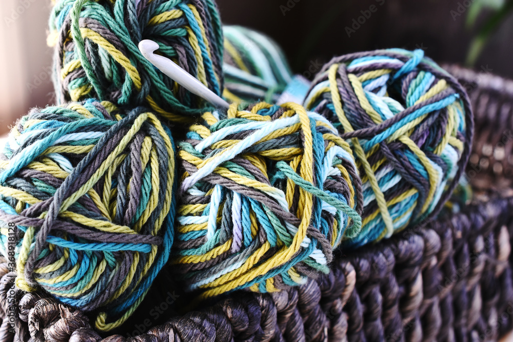 A close up image of several green and brown balls of yarn in a brown wicker basket.