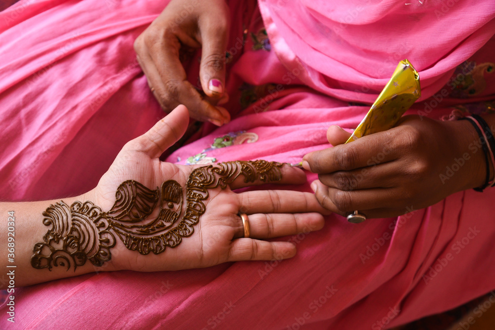 Woman applying beautiful henna, Mehndi tattoo Arabic design on young Indian girls hands at City Palace on wedding in Rajasthan. Mehndi is  popular among women of India, Pakistan, Africa.