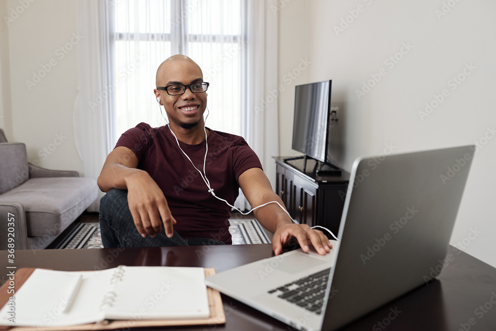 Fototapeta premium Smiling handsome young Black man attending online class or watching webinar on laptop