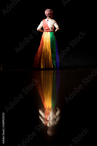 Transgender Asian person doing traditional Indian dance in front of a dark black background. Dressed up like an Indian Goddess.