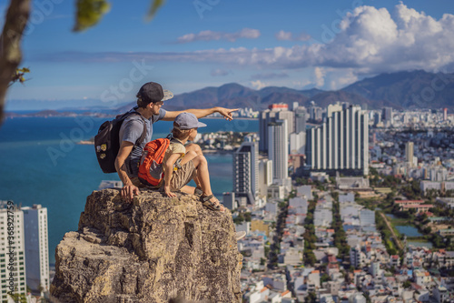 Father and son local tourist sits on a rock and enjoys the view of her city. Local tourism concept. Tourism after COVID 19