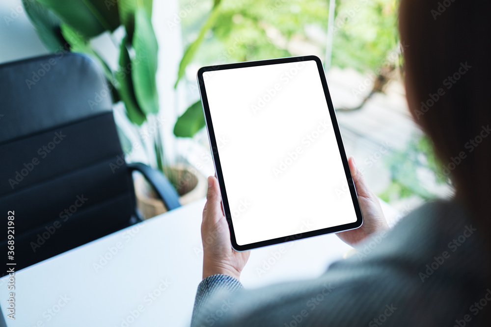 Mockup image of a woman holding digital tablet with blank white desktop screen in the office