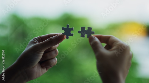 Closeup image of a woman holding and putting a piece of white jigsaw puzzle together with green nature background