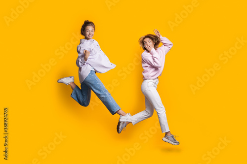 Two jumping caucasian blonde women playing and having fun on yellow studio wall